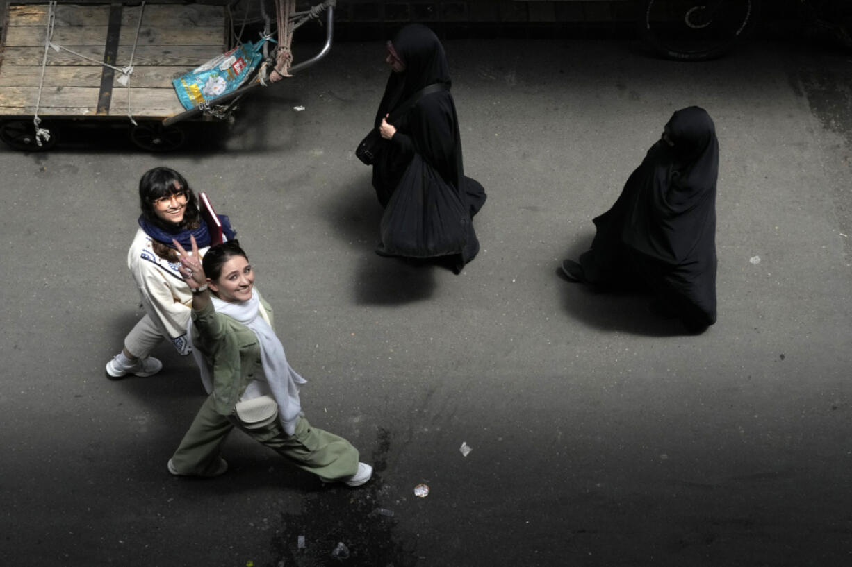 An Iranian woman without wearing her mandatory Islamic headscarf flashes a victory sign as two head-to-toe veiled women walk at the old main bazaar of Tehran, Iran, Thursday, June 13, 2024.