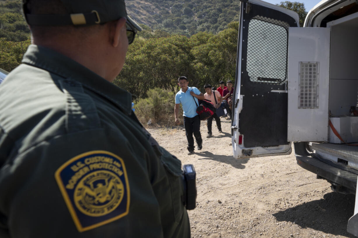 A Border Patrol agent leads a group of migrants seeking asylum towards a van to be transported and processed, Wednesday, June 5, 2024, near Dulzura, Calif. President Joe Biden on Tuesday unveiled plans to enact immediate significant restrictions on migrants seeking asylum at the U.S.-Mexico border as the White House tries to neutralize immigration as a political liability ahead of the November elections.