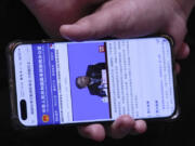 A staff member holding a smartphone showing the State Council Information Office website broadcasting a live of Hu Hao, chief designer of China&rsquo;s Chang&rsquo;e 6 probe speaking during a press conference at the State Council Information Office in Beijing, Thursday, June 27, 2024. China&rsquo;s space officials said Thursday they welcomed scientists from across the world to apply to study the lunar rock samples the Chang&rsquo;e 6 probe brought back to earth in a historic mission, but noted there were limits to that cooperation, specifically with the U.S.