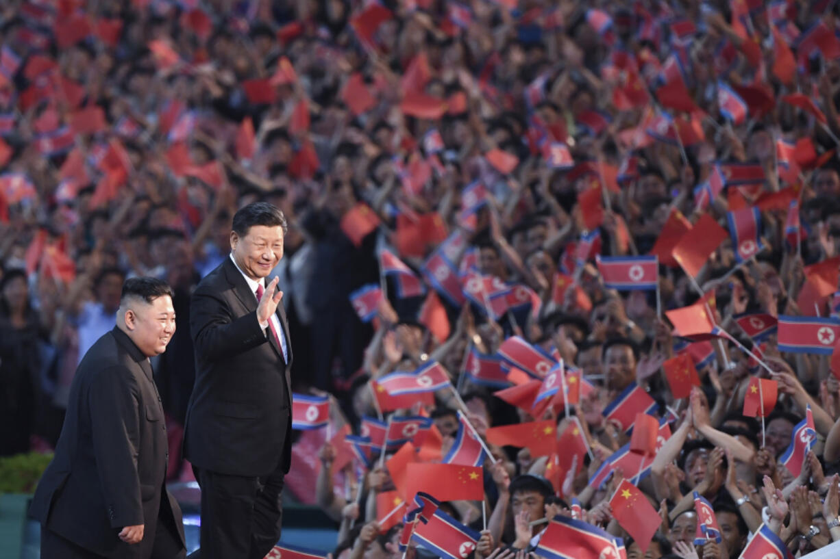 FILE - In this file photo released by China&rsquo;s Xinhua News Agency, spectators wave Chinese and North Korean flags as North Korean leader Kim Jong Un, left, and visiting Chinese President Xi Jinping attend a mass gymnastic performance at the May Day Stadium in Pyongyang, North Korea Thursday, June 20, 2019. China appears to be keeping its distance as Russia and North Korea move closer to each other with a new defense pact that could tilt the balance of power between the three authoritarian states.