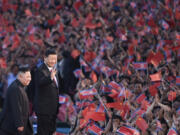 FILE - In this file photo released by China&rsquo;s Xinhua News Agency, spectators wave Chinese and North Korean flags as North Korean leader Kim Jong Un, left, and visiting Chinese President Xi Jinping attend a mass gymnastic performance at the May Day Stadium in Pyongyang, North Korea Thursday, June 20, 2019. China appears to be keeping its distance as Russia and North Korea move closer to each other with a new defense pact that could tilt the balance of power between the three authoritarian states.