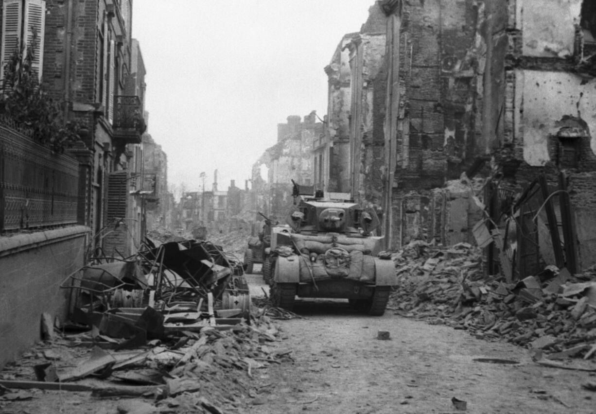 FILE - A British tank makes its way along a street, with the battle still in progress, as the city is still fringed with Nazi guns which continually lob shells into the street, in St. Lo, Normandy, France on June 20, 1944.