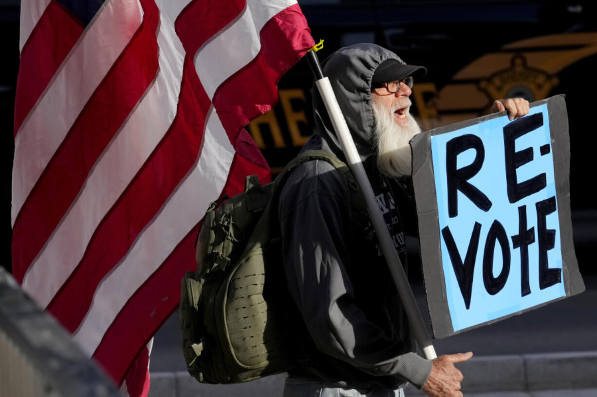 FILE - A man protests outside the Maricopa County Board of Supervisors auditorium prior to the board&#039;s general election canvass meeting, Nov. 28, 2022, in Phoenix. A ghost from recent election cycles, controversies over certification of results, is beginning to re-emerge as the nation heads closer to the 2024 presidential contest.