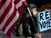 FILE - A man protests outside the Maricopa County Board of Supervisors auditorium prior to the board&#039;s general election canvass meeting, Nov. 28, 2022, in Phoenix. A ghost from recent election cycles, controversies over certification of results, is beginning to re-emerge as the nation heads closer to the 2024 presidential contest.