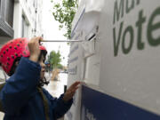 FILE - Ramona McCune, puts vote-by-mail ballots into a dropbox during primary voting on May 21, 2024, in Portland, Ore. Ramona was helping their mom drop off ballots for friends. The Biden campaign is calling on the Republican National Committee and Trump campaign to drop their many lawsuits around the country targeting mail voting.