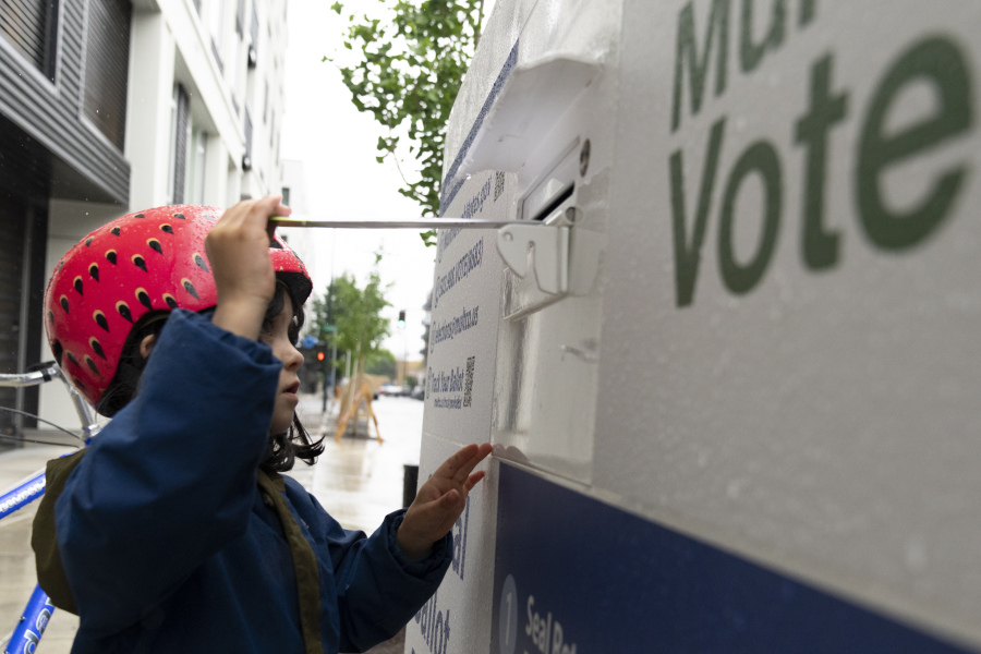 FILE - Ramona McCune, puts vote-by-mail ballots into a dropbox during primary voting on May 21, 2024, in Portland, Ore. Ramona was helping their mom drop off ballots for friends. The Biden campaign is calling on the Republican National Committee and Trump campaign to drop their many lawsuits around the country targeting mail voting.