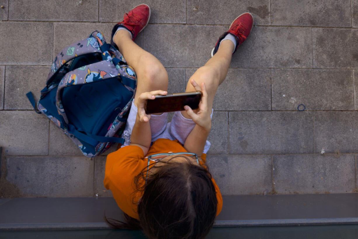 A 11-year-old boy plays with his father&rsquo;s phone outside school in Barcelona, Spain, Monday, June 17, 2024. Parents across Europe are rallying to make it normal for young kids to live smartphone-free. From Spain to Ireland and the UK, groups are ballooning on chat groups like WhatsApp and agreeing to link arms and refuse to buy children younger than 12 smartphones.