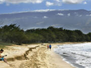 FILE -- Snow-capped Haleakala serves as a backdrop as Paia, Maui&rsquo;s Scott Picton, left, plays a guitar and Saskatchewan&rsquo;s Shannon and Dan Runcie walk on Sugar Beach in South Maui, Hawaii, Feb. 11, 2019. Local officials on the Hawaiian island of Maui on Wednesday, June 5, 2024, voted to oppose a U.S. military proposal to build new telescopes on the summit of Haleakala volcano.