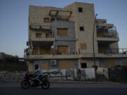 A man drives his motorcycle past a damaged building, from previous shelling attacks from Lebanon, in Kiryat Shmona, northern Israel, Wednesday, June 19, 2024. Hezbollah began attacking Israel almost immediately after the Israel-Hamas war erupted on Oct. 7. There have been near daily exchanges of fire, though most of the strikes are confined to an area within a few mostly confined to the area around the border.