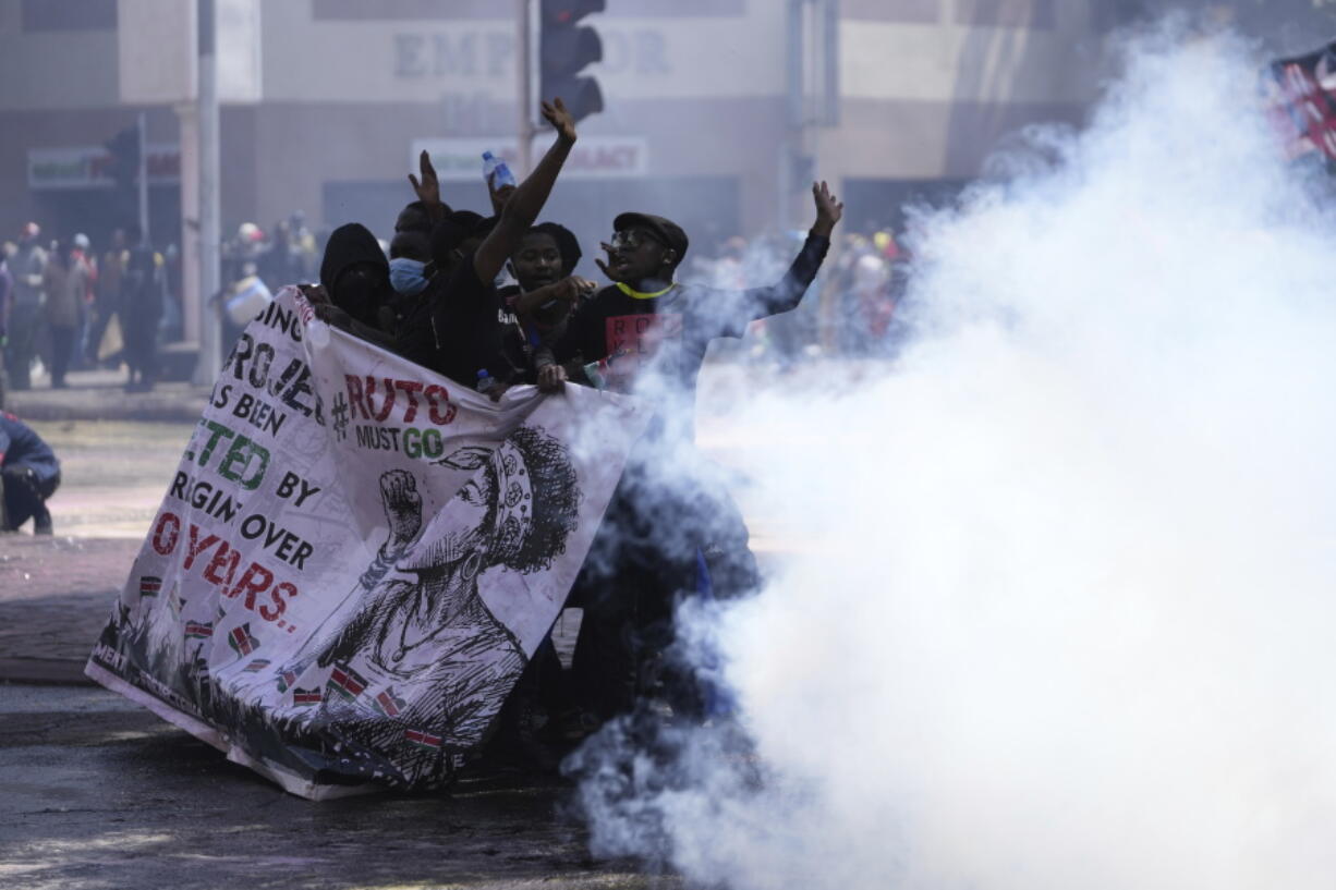 Protesters hide behind a banner as police fire teargas at them during a protest over proposed tax hikes in a finance bill in downtown Nairobi, Kenya Tuesday, June 25, 2024.