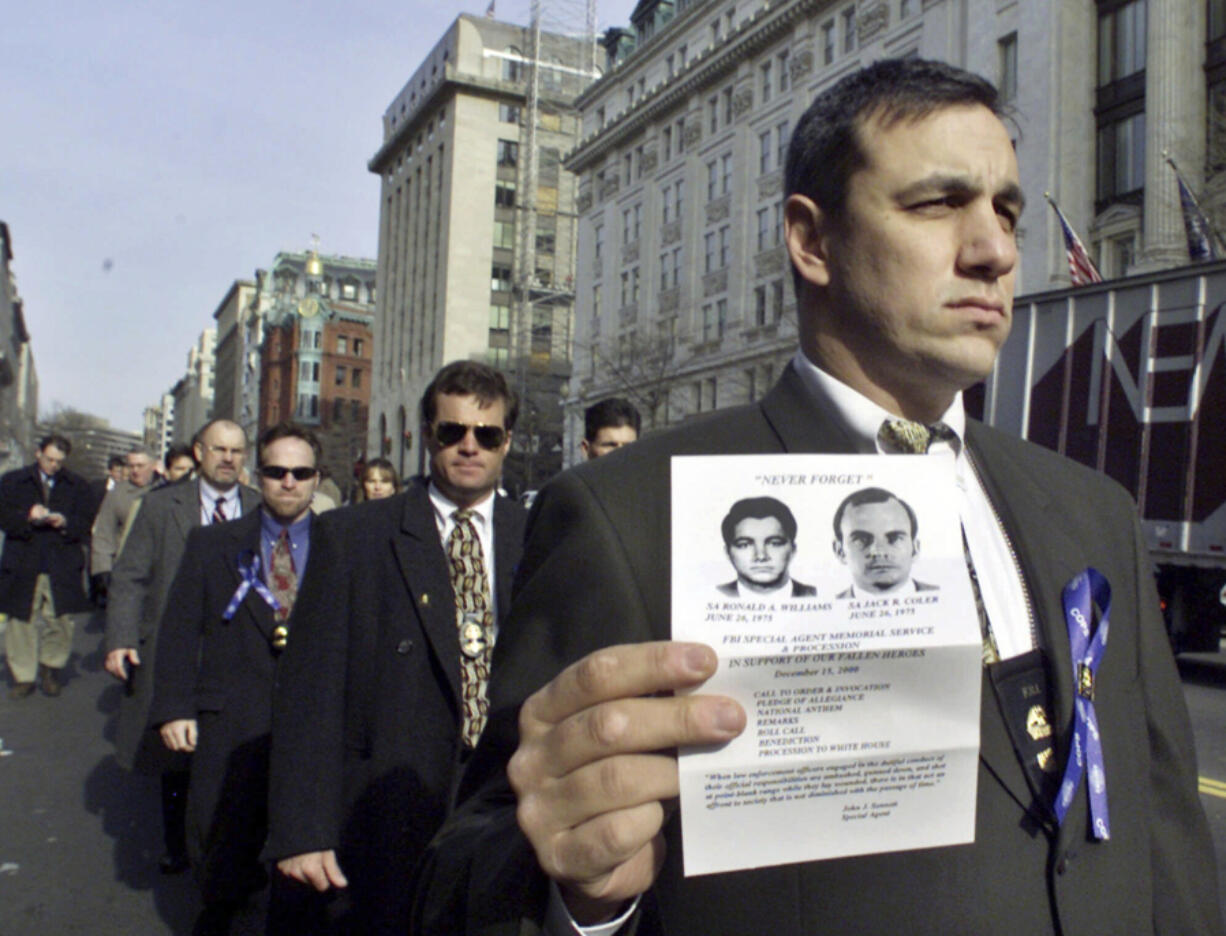 FILE - An unidentified FBI agent, one of the nearly 500 current and retired FBI agents protesting clemency for Leonard Peltier, marches toward the White House, Friday, Dec. 15, 2000, holding an image of two FBI agents, Ron Williams and Jack Coler, who were killed on the Pine Ridge Indian reservation in South Dakota in 1975. Peltier, who has spent most of his life in prison for the killings, has a parole hearing Monday, June 10, 2024, at a federal prison in Florida.