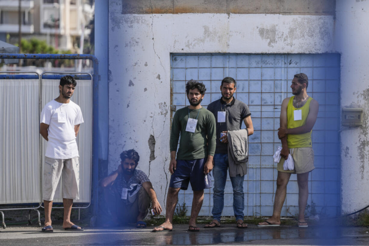 FILE - Survivors of a shipwreck stand outside a warehouse at the port in Kalamata town, about 240 kilometers (150miles) southwest of Athens, Greece, Thursday, June 15, 2023. A year after one of the worst migrant boat tragedies in the Mediterranean Sea, there are only hazy answers as to why hundreds of lives were lost and who can be held answerable. Survivors say they are still waiting for justice, while bearing the trauma of the shipwreck and the horrible five-day journey that preceded it.