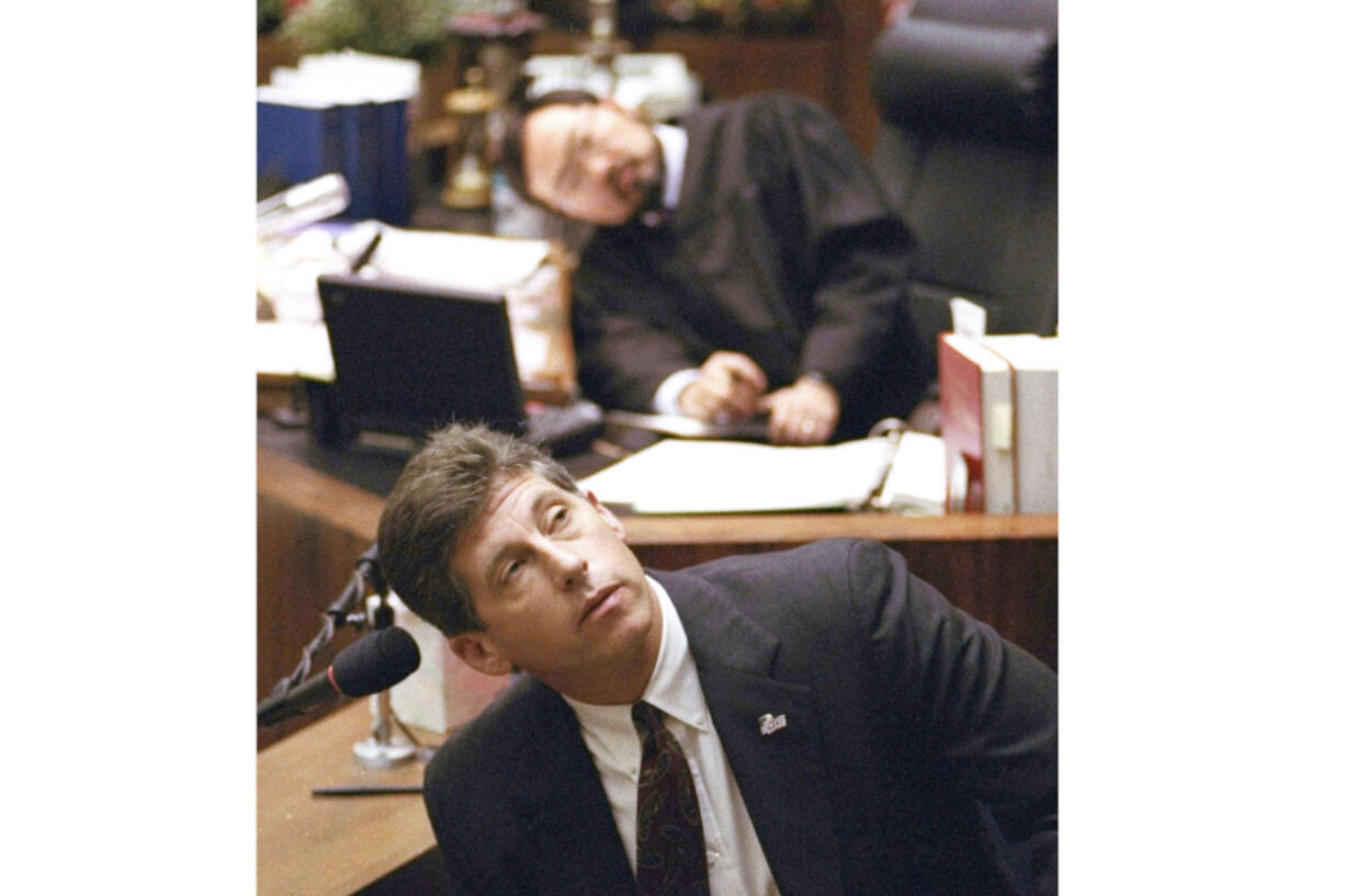 FILE - Los Angeles Police Department Det. Mark Fuhrman, foreground, and Superior Court Judge Lance Ito, rear, crane their heads to look at an overhead monitor during the O.J. Simpson double-murder trial, Friday, March 10, 1995, in Los Angeles. Fuhrman, 72, who was convicted of lying on the witness stand in the O.J. Simpson trial three decades ago, is now barred from law enforcement under a California police reform law meant to strip the badges of police officers who act criminally or with bias.