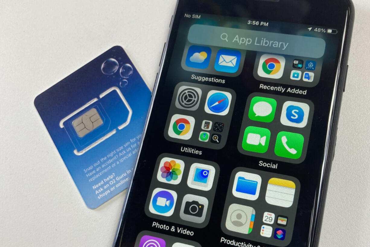 A SIM card is shown next to a cellphone in this photo taken on Tuesday, June 11, 2024 in London. Physical SIM cards are going away, replaced by eSIMs which make switching cell carriers easier.