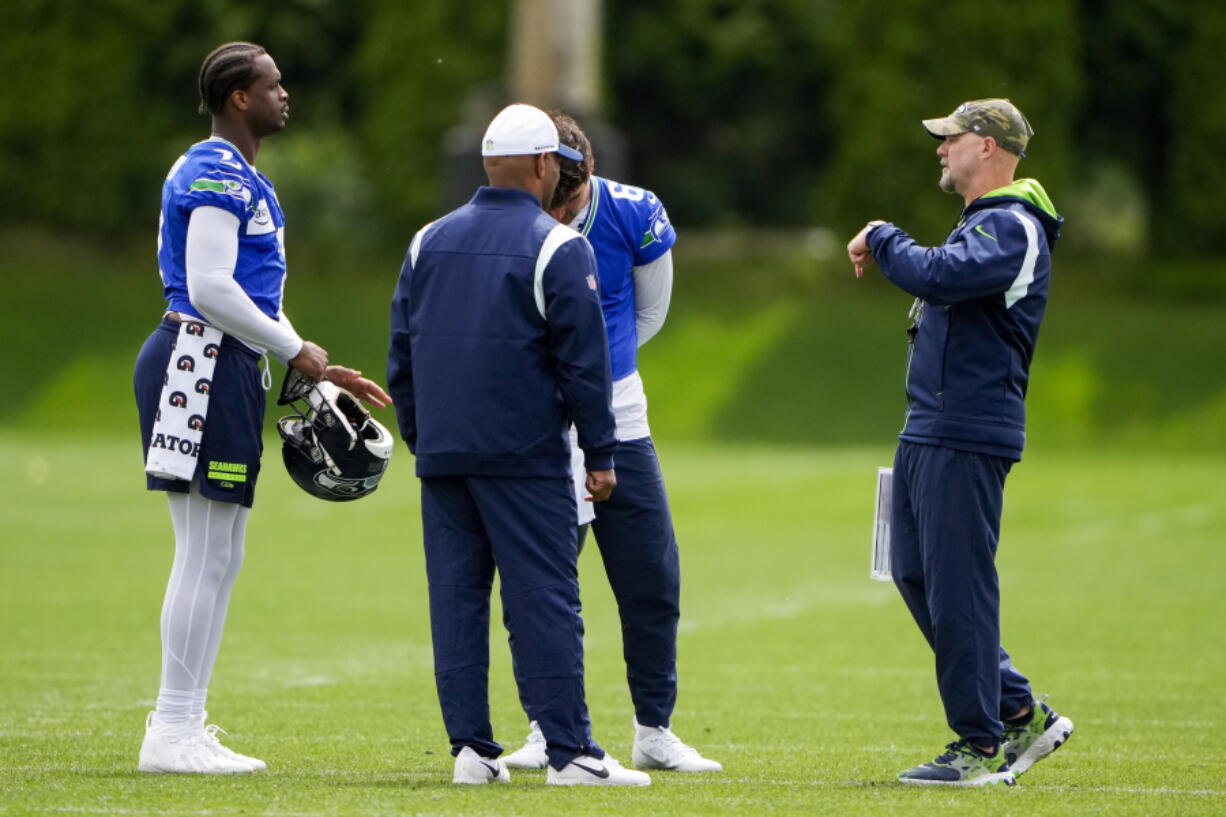 Seattle Seahawks quarterbacks Geno Smith, left, and Sam Howell, back center, stand with quarterbacks coach Charles London, front center, and offensive coordinator Ryan Grubb, right, during an NFL football practice, Monday, June 3, 2024, in Renton, Wash.