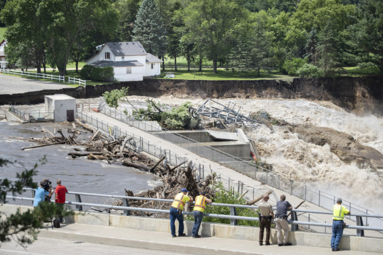 Onlookers take in the catastrophic damage to the Rapidan Dam site in Rapidan, Minn., Monday, June 24, 2024. Debris blocked the dam forcing the heavily backed up waters of the Blue Earth River to reroute along the bank nearest the Dam Store.