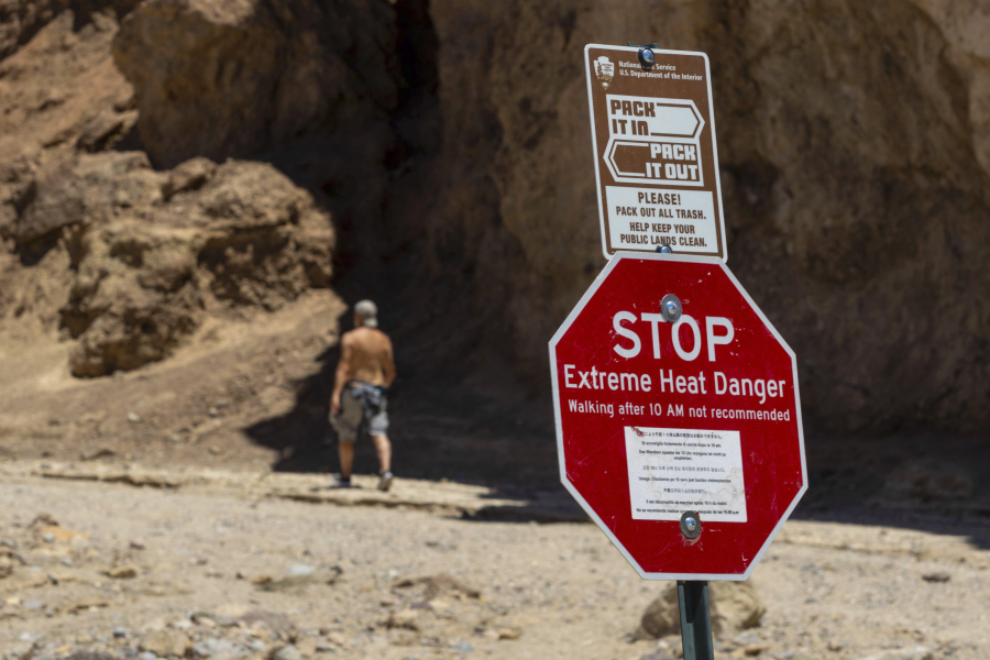 FILE - A hiker passes a sign warning of extreme heat at the start of the Golden Canyon trail, in Death Valley National Park, Calif.,  July 11, 2023. Parts of California, Nevada and Arizona are expected to bake this week as the first heat wave of the season arrives with triple-digit temperatures forecast for areas including Phoenix, which last summer saw a record 31 straight days of at least 110 degrees Fahrenheit (43.3 Celsius).