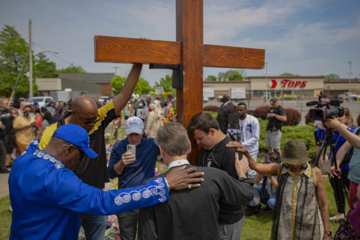 A group prays May 21, 2022, at the site of a memorial for the victims of a shooting outside the Tops Friendly Markets in Buffalo, N.Y.