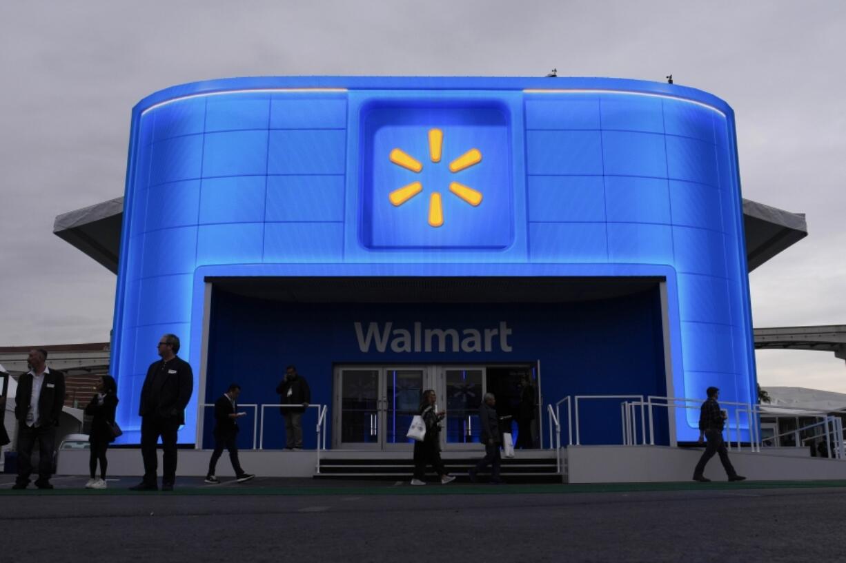 FILE - People walk by the Walmart booth during the CES tech show Tuesday, Jan. 9, 2024, in Las Vegas. Walmart is offering new perks for its hourly workers. They include a new bonus plan as well as opportunities to move into skilled trade jobs within the company.