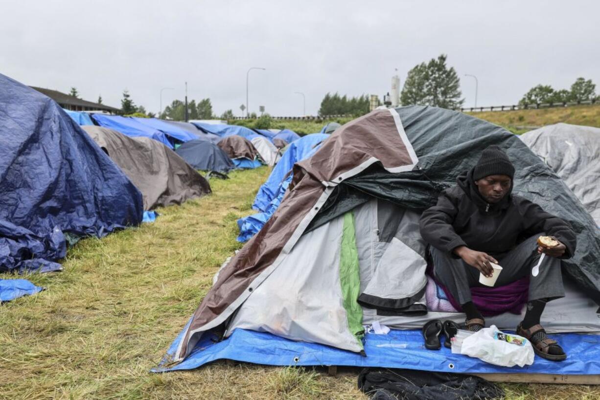 Kunau Eyumu Thierry sits outside his family tent at a camp on Tuesday, June 4, 2024, in Kent, Wash. Asylum seekers who have been looking for shelter in Washington state, mainly from Angola, Congo and Venezuela, have set up an encampment in a Seattle suburb.