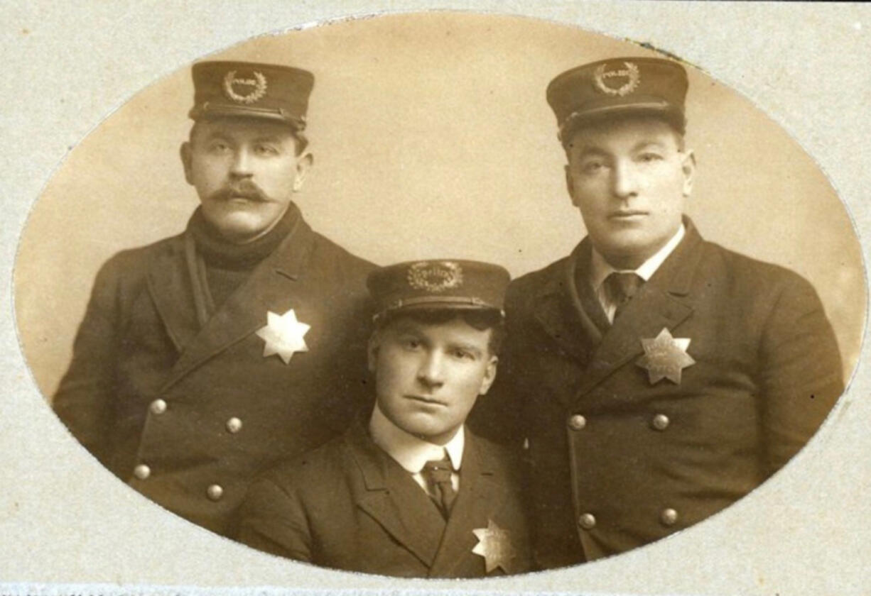 Taken before 1908, this photograph shows early Vancouver policemen &mdash; Winfield Gasaway, Henry Burgy and John Secrist &mdash; wearing their seven-pointed badges and caps with curved olive branches. Burgy and Secrist would go on to serve as Vancouver police chiefs.