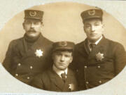 Taken before 1908, this photograph shows early Vancouver policemen &mdash; Winfield Gasaway, Henry Burgy and John Secrist &mdash; wearing their seven-pointed badges and caps with curved olive branches. Burgy and Secrist would go on to serve as Vancouver police chiefs.