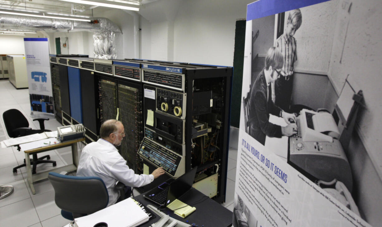 In this photo taken Oct. 30, 2012, Bruce Sherry, a contract engineer at the Living Computer Museum in Seattle, manually programs a DEC PDP-10 computer from the early 1970s next to a photograph of Microsoft co-founders Paul Allen, seated, and Bill Gates, standing at Allen&rsquo;s left, working on a teletype machine. Allen has just opened the Living Computer Museum, which features working models of old computers. (AP Photo/Ted S.