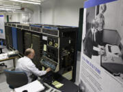 In this photo taken Oct. 30, 2012, Bruce Sherry, a contract engineer at the Living Computer Museum in Seattle, manually programs a DEC PDP-10 computer from the early 1970s next to a photograph of Microsoft co-founders Paul Allen, seated, and Bill Gates, standing at Allen&rsquo;s left, working on a teletype machine. Allen has just opened the Living Computer Museum, which features working models of old computers. (AP Photo/Ted S.