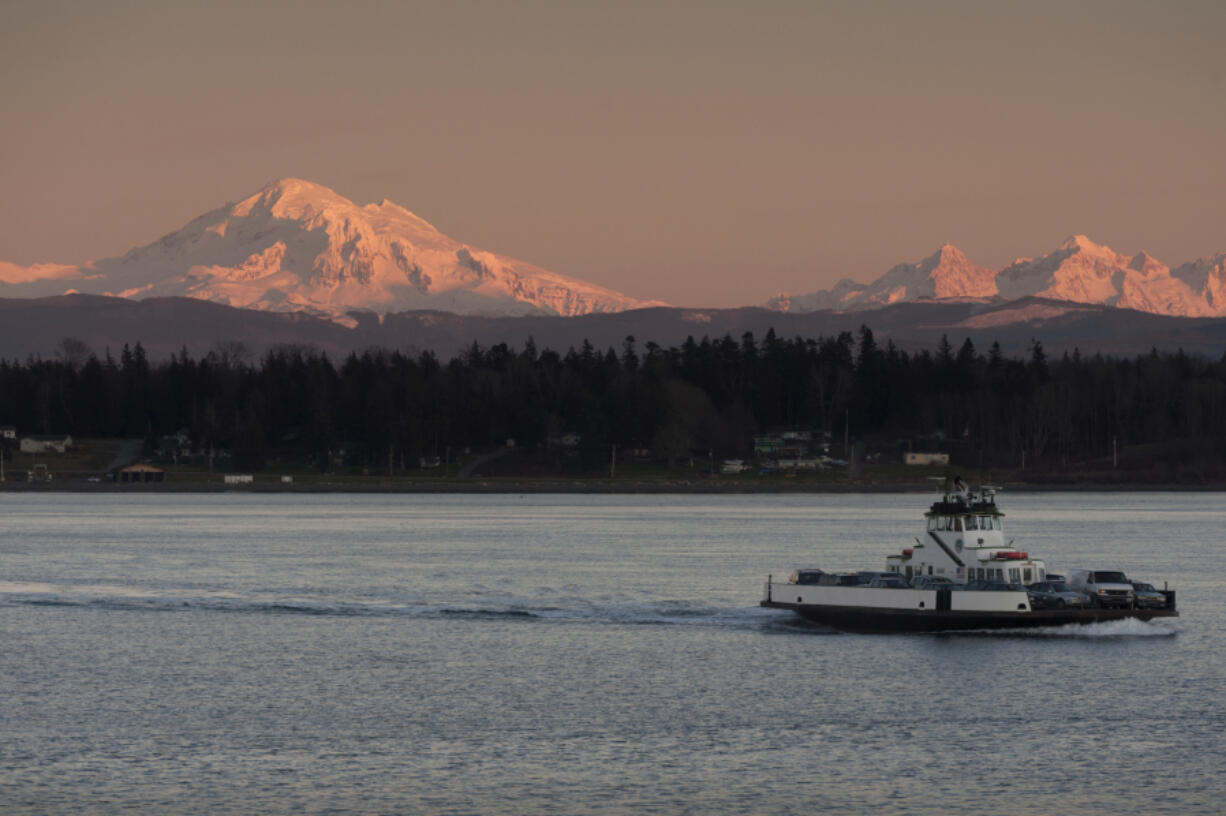 A ferry boat crosses the Puget Sound while Mount Baker looms in the background at sunset.