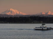 A ferry boat crosses the Puget Sound while Mount Baker looms in the background at sunset.