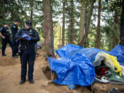 Officer Zach Rosling and other Vancouver police respond to a call of a dead body at a homeless encampment near Hazel Dell in April. The Vancouver City Council voted to put a levy lid left on the November ballot to add more police resources.