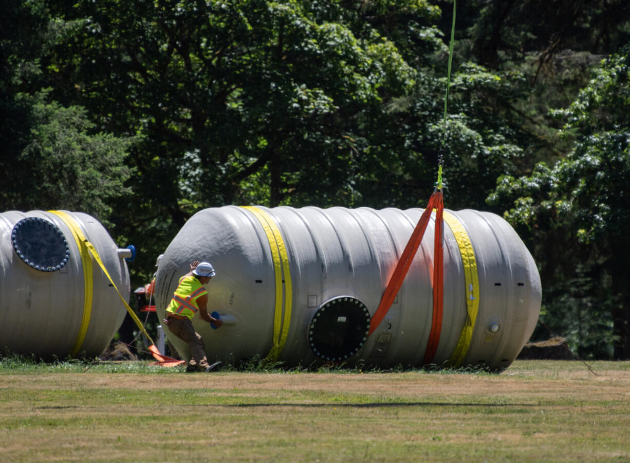 Workers secure straps around water tanks Wednesday at Lewisville Regional Park near Battle Ground. The tanks were delivered via helicopter to Camp Hope of Southwest Washington.
