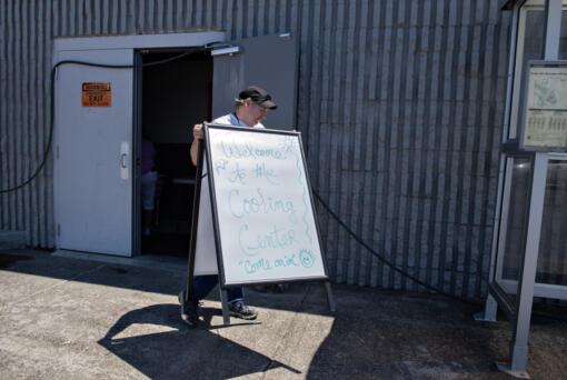 Worship team volunteer David Leitz sets out a sign to welcome guests to the Living Hope Church cooling center Monday afternoon as temperatures climbed to triple digits outside.