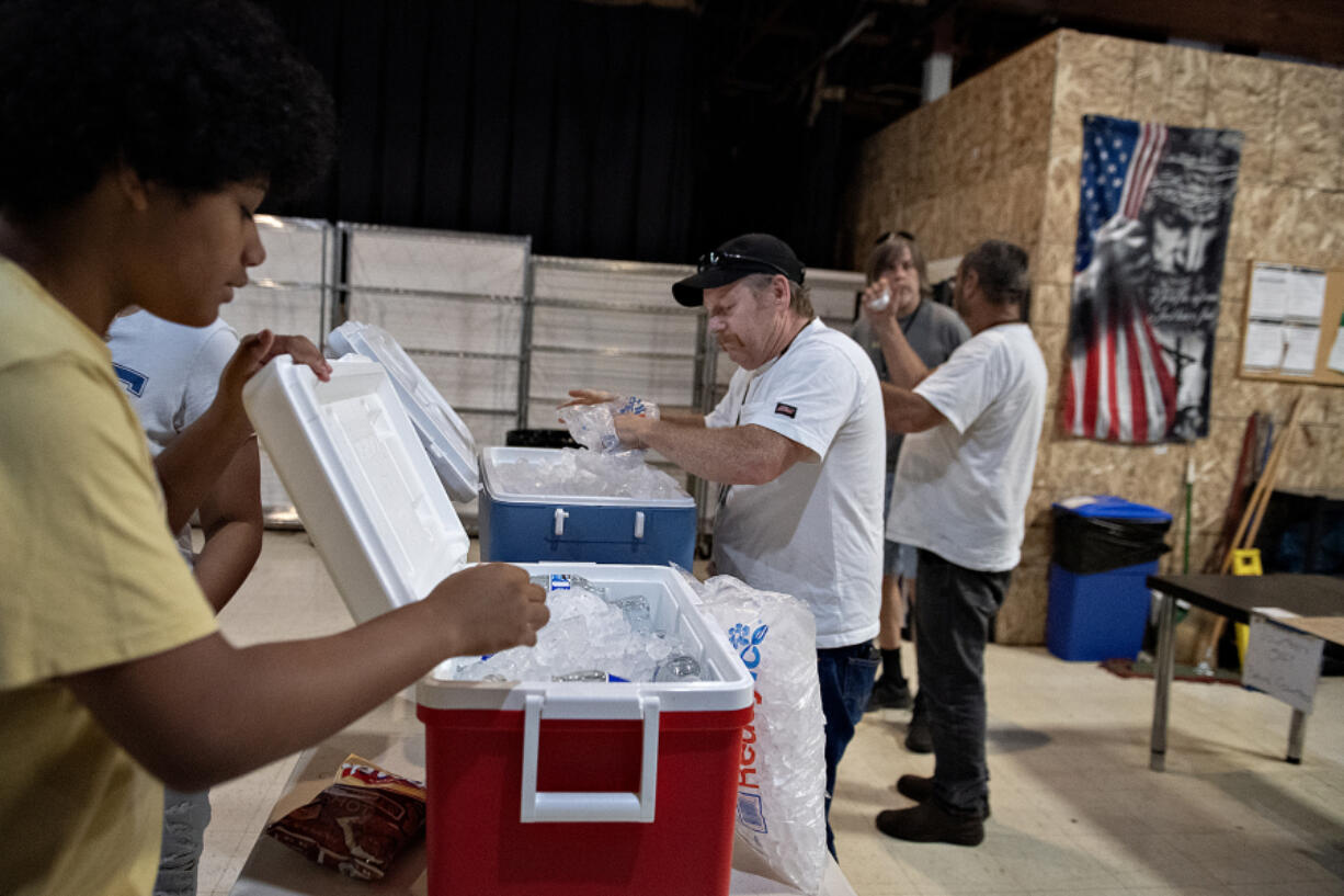 Volunteer Keith Dewing, left, and David Leitz prepare coolers of ice water for guests at the Living Hope Church cooling center Monday afternoon.