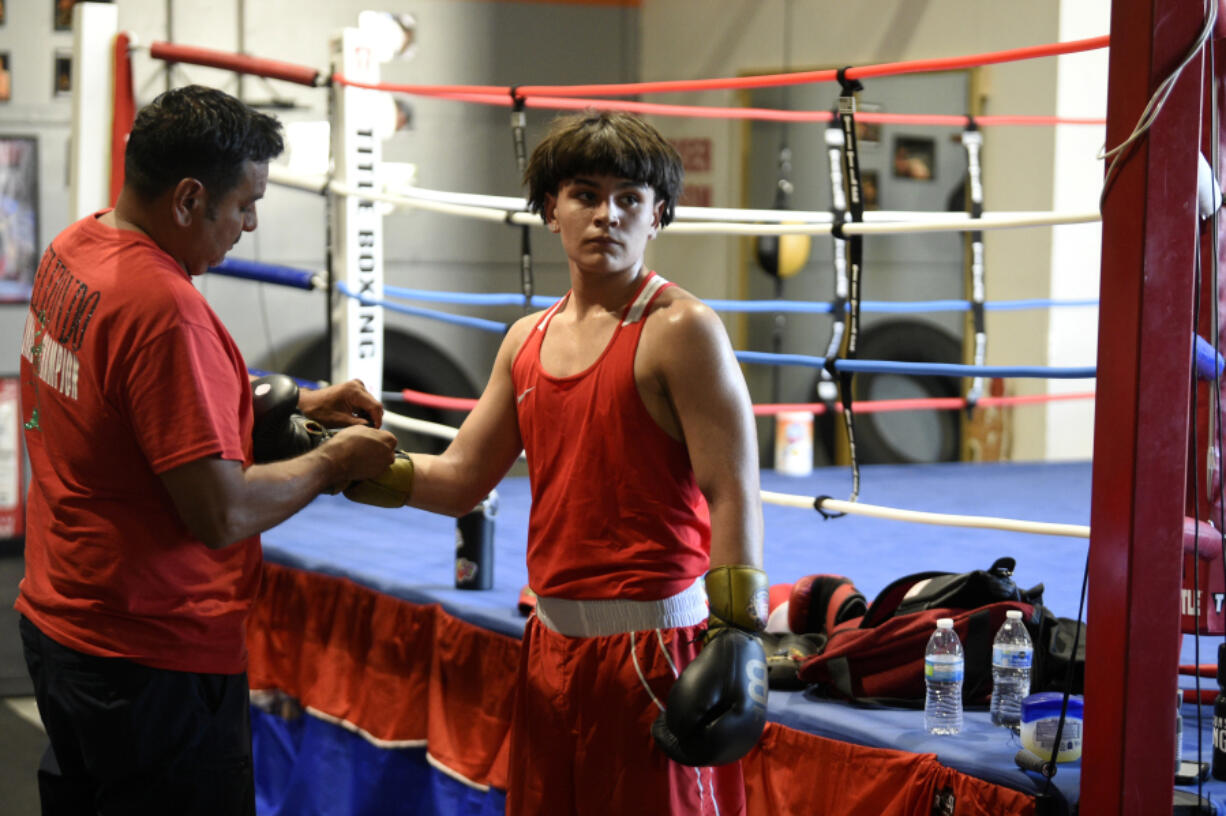 Cain Elizondo, left, laces up boxing gloves for his son, Cain Elizondo Jr., at Young Guns Boxing in Hazel Dell on Wednesday, July 17, 2024. Elizondo Jr., 14, is the nation&rsquo;s top-ranked 125-pounder in his age group in the USA Boxing national rankings.