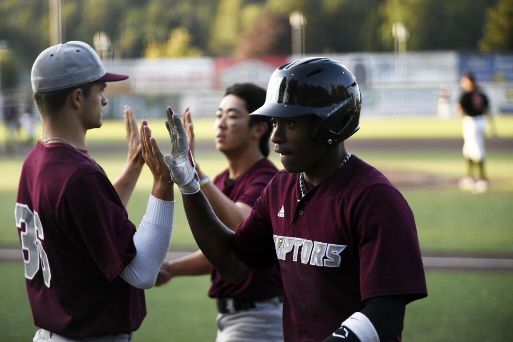 Dasan Harris (foreground) and Taylor Takata (background) of the Ridgefield Raptors are greeted by teammate Curtis Hebert (36) after scoring in the Raptors' West Coast League baseball game against the Cowlitz Black Bears at David Story Field in Longview on Friday, July 26, 2024.