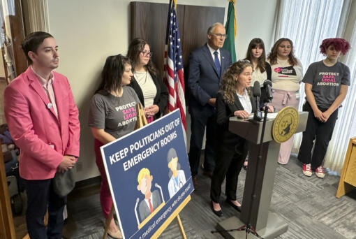Washington Gov. Jay Inslee, center rear, and abortion rights supporters listen as Dr. Sarah Prager, a professor of obstetrics and gynecology at the University of Washington, speaks to reporters during a news conference in Seattle, Tuesday, June 11, 2024. Inslee announced that Washington state will spell out in state law that hospitals must provide abortions if needed to stabilize patients, a step that comes as the U.S. Supreme Court is expected to rule this month on whether conservative states can bar abortions during some medical emergencies.