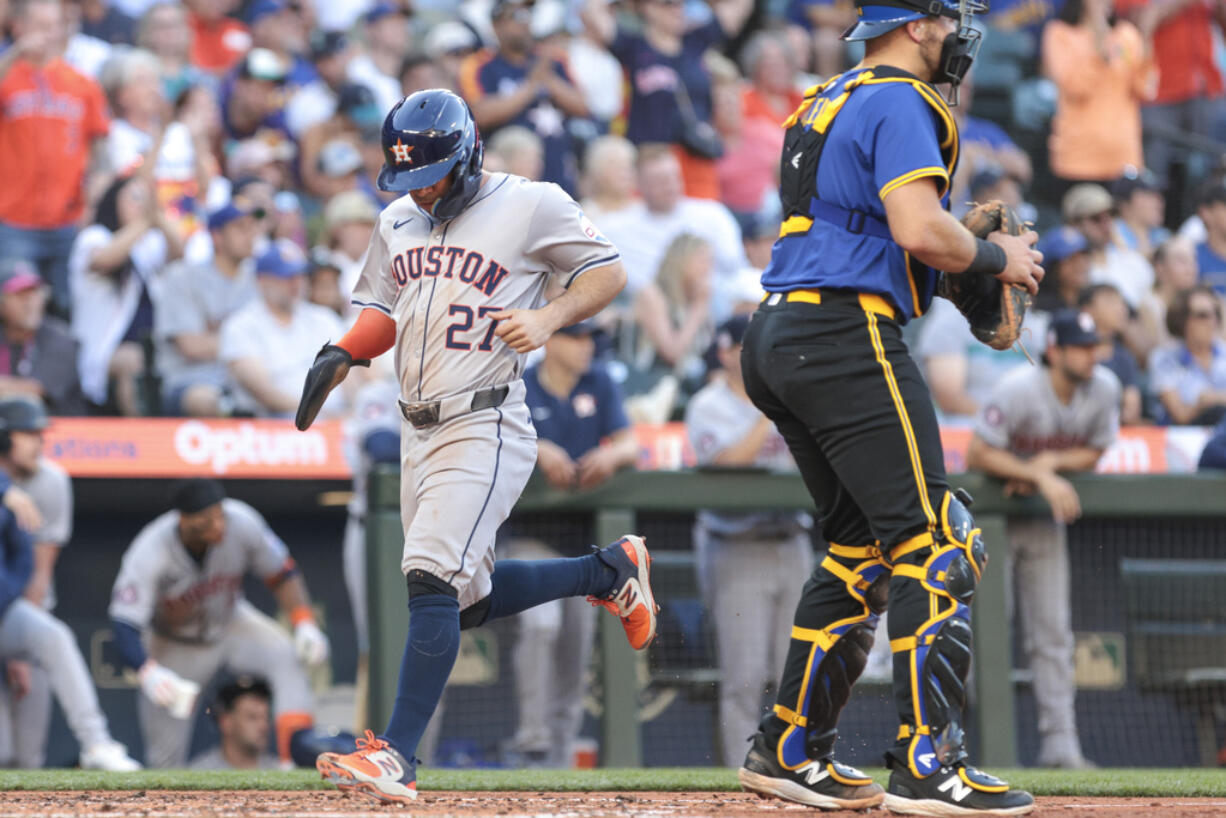 Houston Astros' Jose Altuve (27) scores on a two-RBI single by Yainer Diaz as Seattle Mariners catcher Cal Raleigh, right, looks on during the third inning of a baseball game Friday, July 19, 2024, in Seattle.