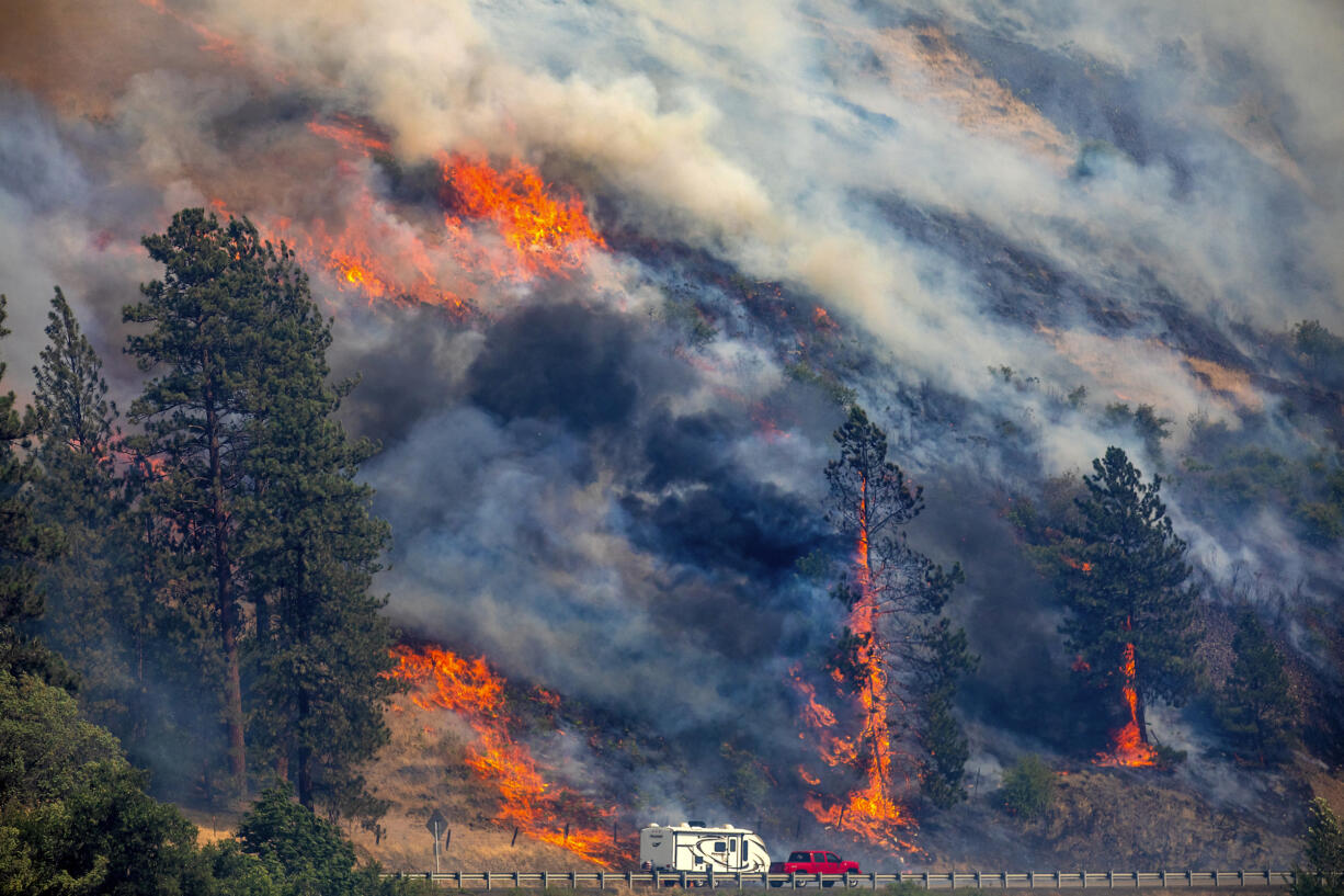 A vehicle drives past the spreading River Fire Thursday, July 25, 2024, near Myrtle, Idaho, before U.S. Highway 12 was closed. Lightning strikes have sparked fast-moving wildfires in Idaho, prompting the evacuation of multiple communities.