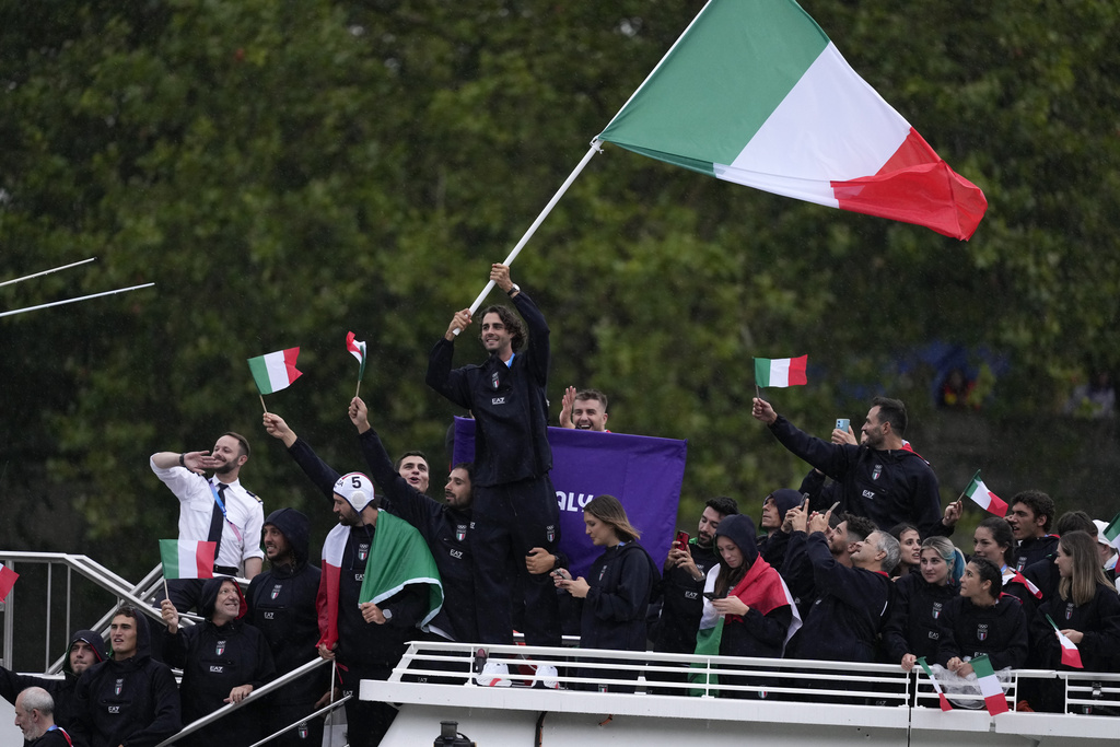 Gianmarco Tamberi waves an Italian flag as the Italian team parades along the Seine river in Paris, France, during the opening ceremony of the 2024 Summer Olympics, Friday, July 26, 2024 (AP Photo/Luca Bruno)