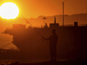 A man fishes off a jetty in Alameda, Calif., as the sun sets over the San Francisco Bay on Monday, July 1, 2024. An extended heatwave predicted to blanket Northern California has resulted in red flag fire warnings and the possibility of power shutoffs beginning Tuesday.