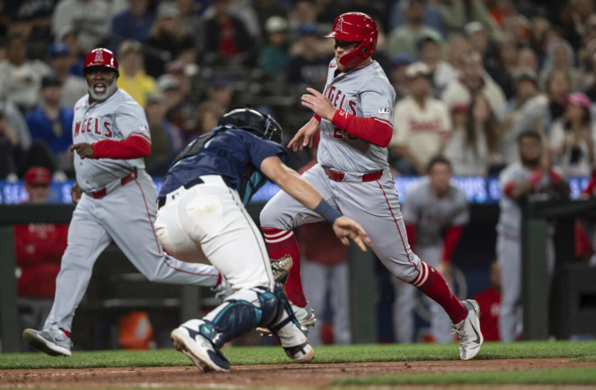 Los Angeles Angels&#039; Brandon Drury, right, runs past Seattle Mariners catcher Cal Raleigh, center, to score a run during the ninth inning of a baseball game Monday, July 22, 2024, in Seattle.