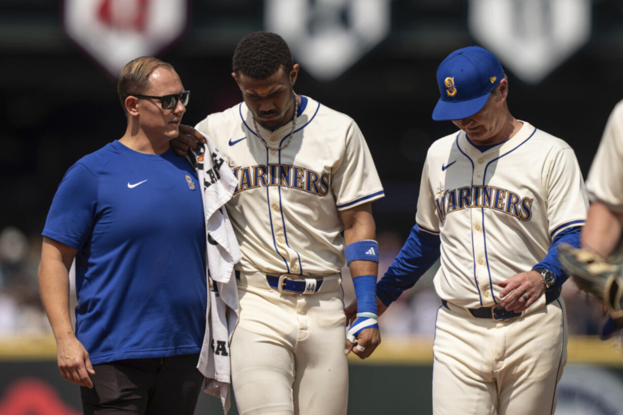 Seattle Mariners centerfielder Julio Rodriguez, center, is helped from the field by manager Scott Servais, right, and a team trainer during the sixth inning of a baseball game against the Houston Astros, Sunday, July 21, 2024, in Seattle.