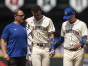 Seattle Mariners centerfielder Julio Rodriguez, center, is helped from the field by manager Scott Servais, right, and a team trainer during the sixth inning of a baseball game against the Houston Astros, Sunday, July 21, 2024, in Seattle.