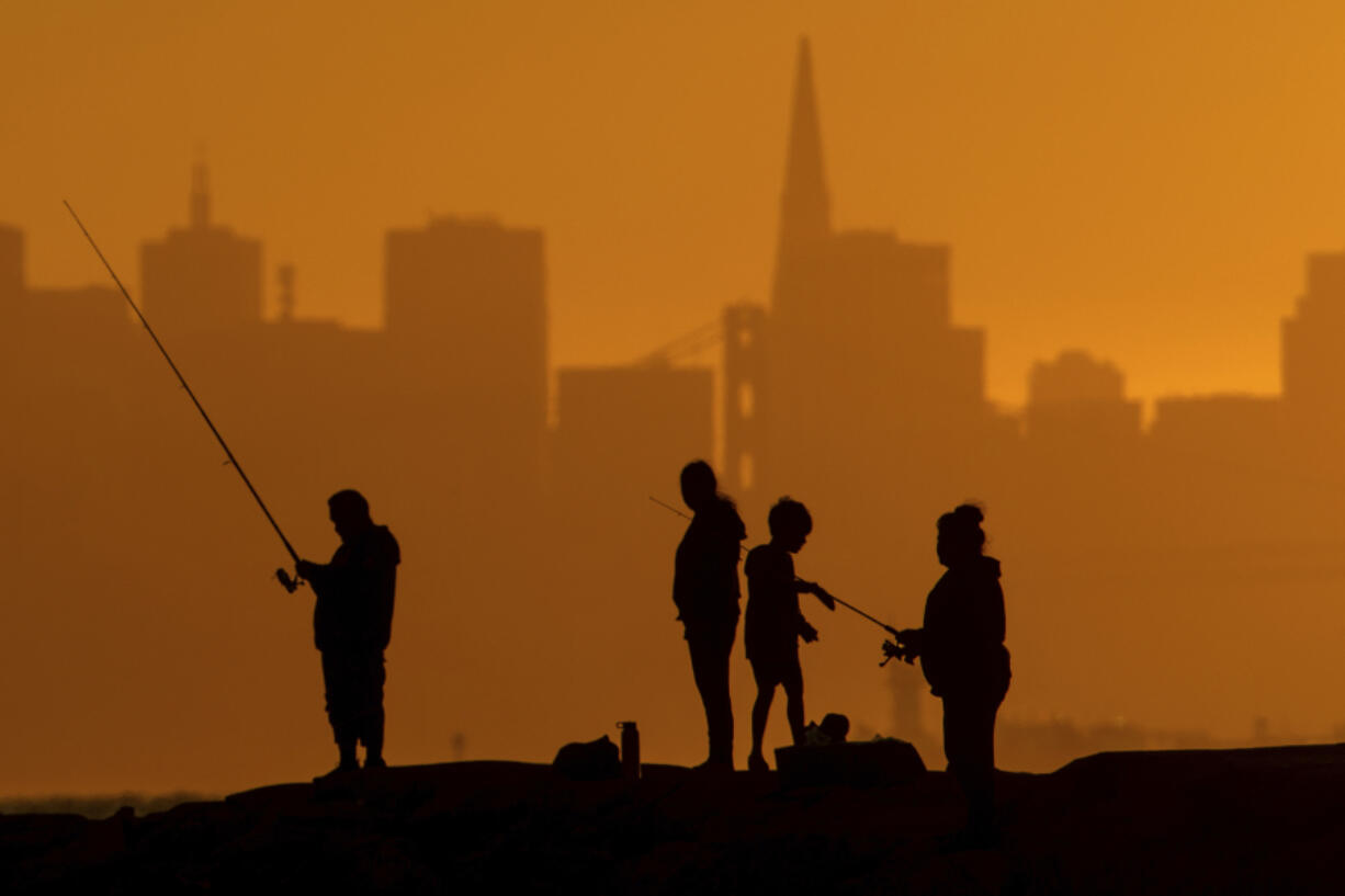 With the San Francisco skyline behind them, people fish off a jetty Monday, July 1, 2024, in Alameda, Calif. An extended heatwave predicted to blanket Northern California has resulted in red flag fire warnings and the possibility of power shutoffs beginning Tuesday.