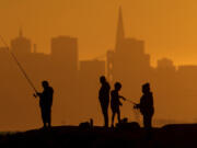 With the San Francisco skyline behind them, people fish off a jetty Monday, July 1, 2024, in Alameda, Calif. An extended heatwave predicted to blanket Northern California has resulted in red flag fire warnings and the possibility of power shutoffs beginning Tuesday.