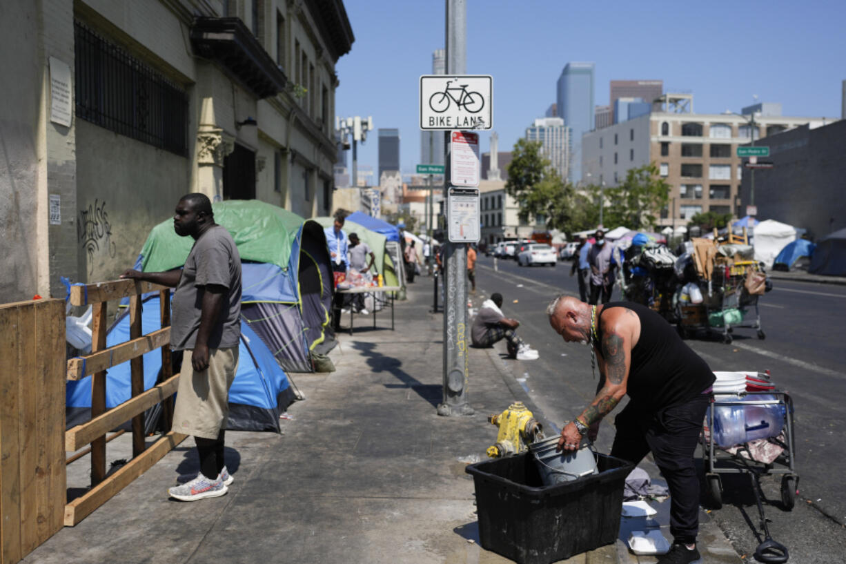 Two men work and stand on a sidewalk on Skid Row, Thursday, July 25, 2024, in Los Angeles. California Gov. Gavin Newsom issued an executive order Thursday to direct state agencies on how to remove homeless encampments, a month after a Supreme Court ruling allowing cities to enforce bans on sleeping outside in public spaces. (AP Photo/Jae C.