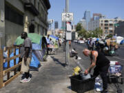 Two men work and stand on a sidewalk on Skid Row, Thursday, July 25, 2024, in Los Angeles. California Gov. Gavin Newsom issued an executive order Thursday to direct state agencies on how to remove homeless encampments, a month after a Supreme Court ruling allowing cities to enforce bans on sleeping outside in public spaces. (AP Photo/Jae C.