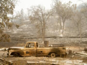 A charred vehicle rests below a hill in Paynes Creek after the Park Fire burned through the community in Tehama County, Calif., on Saturday, July 27, 2024.