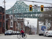 FILE - A cyclist rides along a street near the Tobin Memorial Bridge, background, in Chelsea, Mass., on Wednesday, March 31, 2021. After nearly 1,750 low-income people in the Boston suburb won a lottery to receive monthly stipends from the city from November 2020 to August 2021, researchers found that winners visited emergency departments significantly less than people who did not receive the monthly payments.